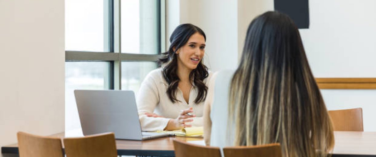 The young adult  business owner gestures as she asks the unrecognizable female job applicant questions during the interview.